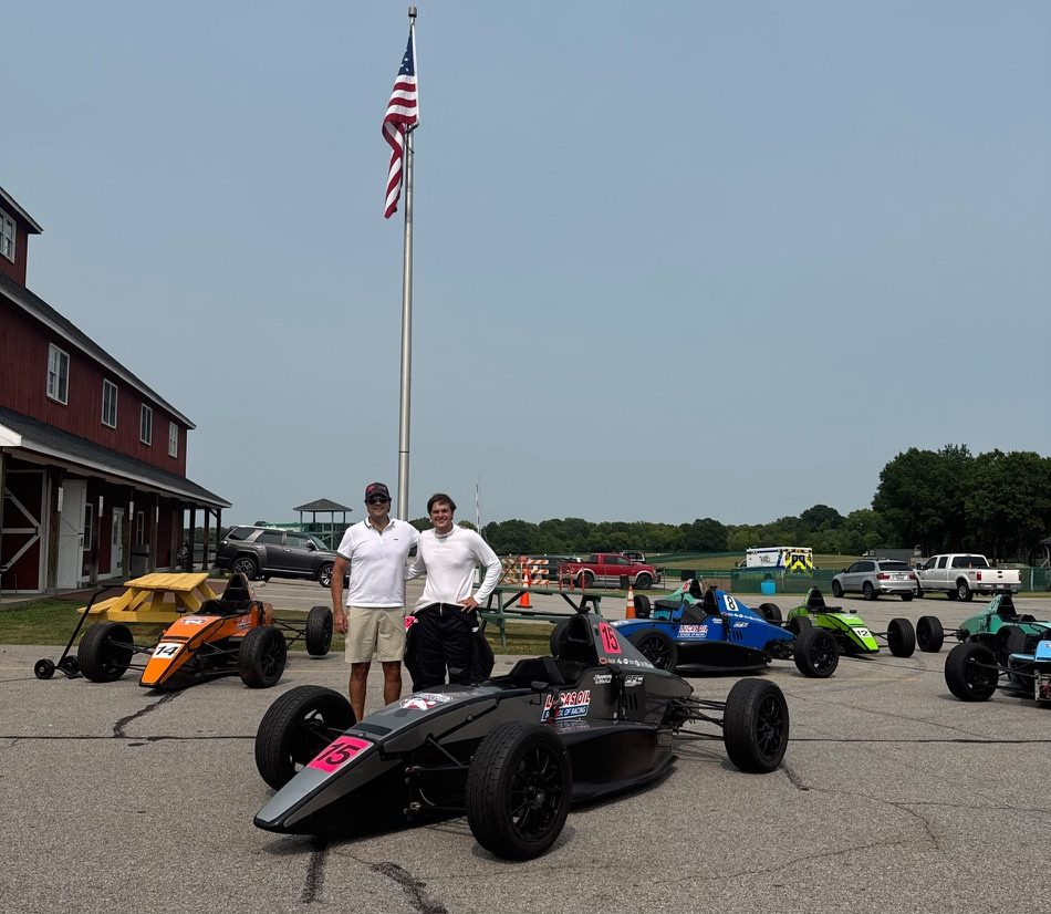 Sergio Ostos with the #15 car and a row of formula cars in the paddock